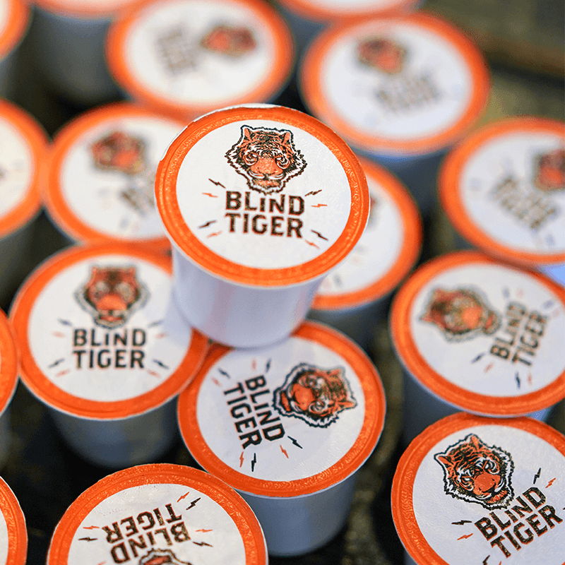 Multiple coffee pods with 'Blind Tiger' branding on a blurred background