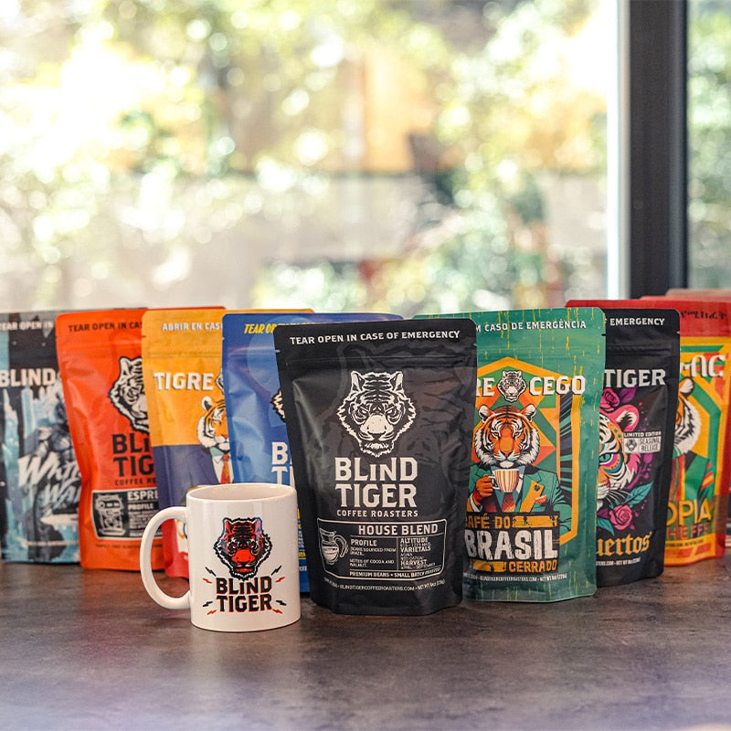 Collection of Blind Tiger coffee packages and a mug on a surface with a blurred window background.