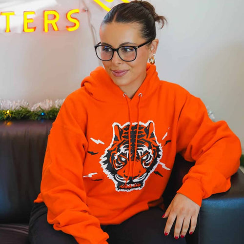 Person wearing an orange hoodie with a tiger design, sitting on a couch in a casual setting.