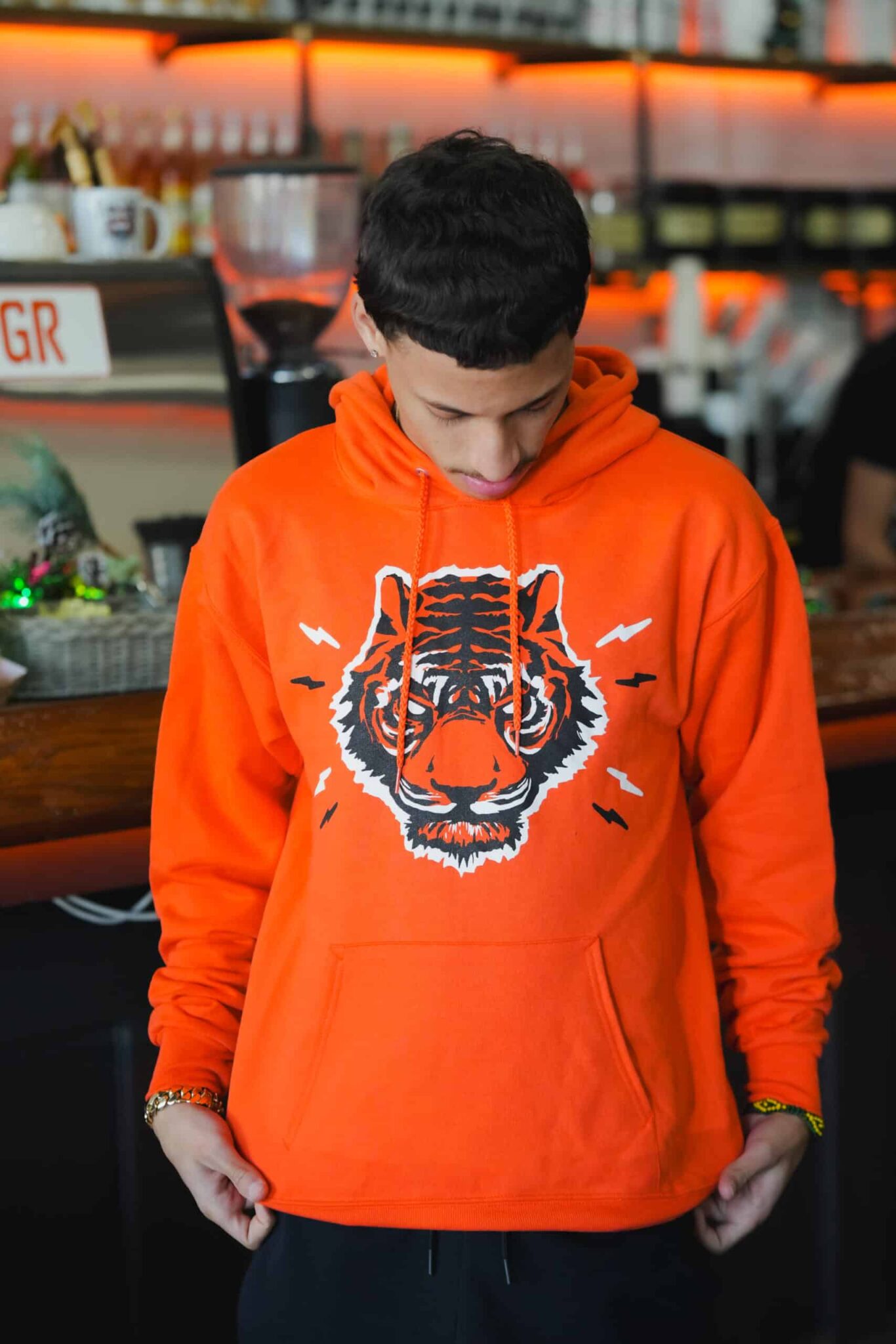 Person wearing an orange hoodie with a tiger design in a casual setting