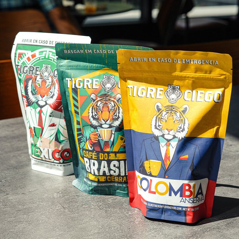 Three colorful coffee bags with tiger illustrations and country names on a gray surface.